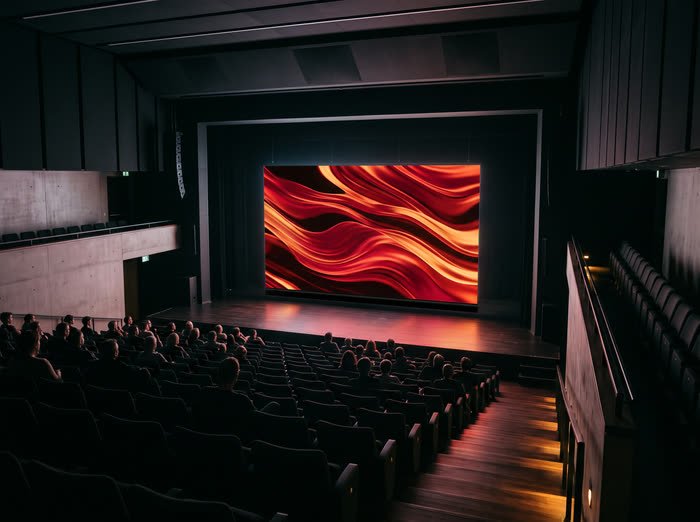 Wide roll-down LED video wall glowing over the stage of a dark auditorium